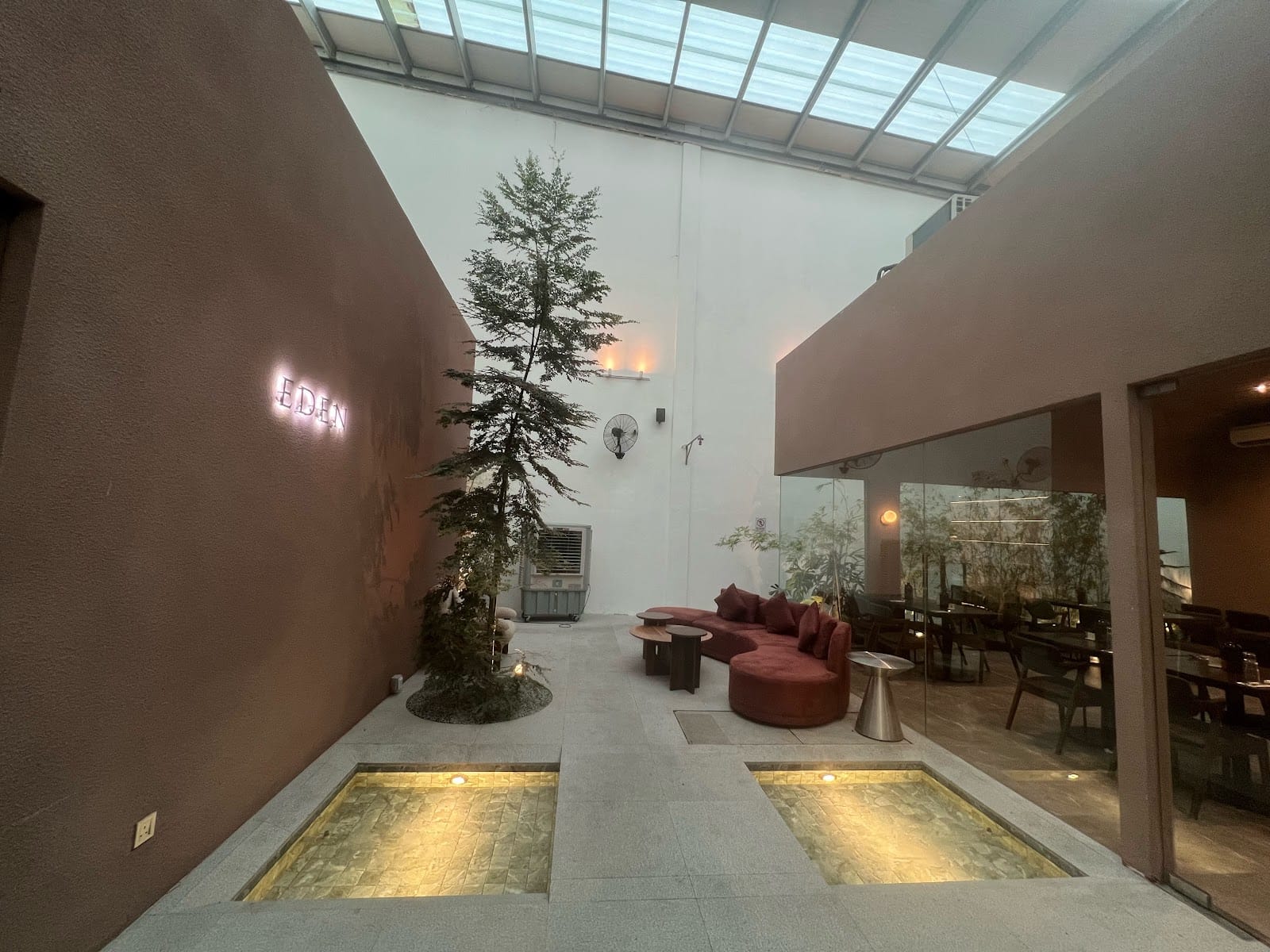 The skylit atrium: a tall tree, two lit pools and a curved red sofa beside the dining room