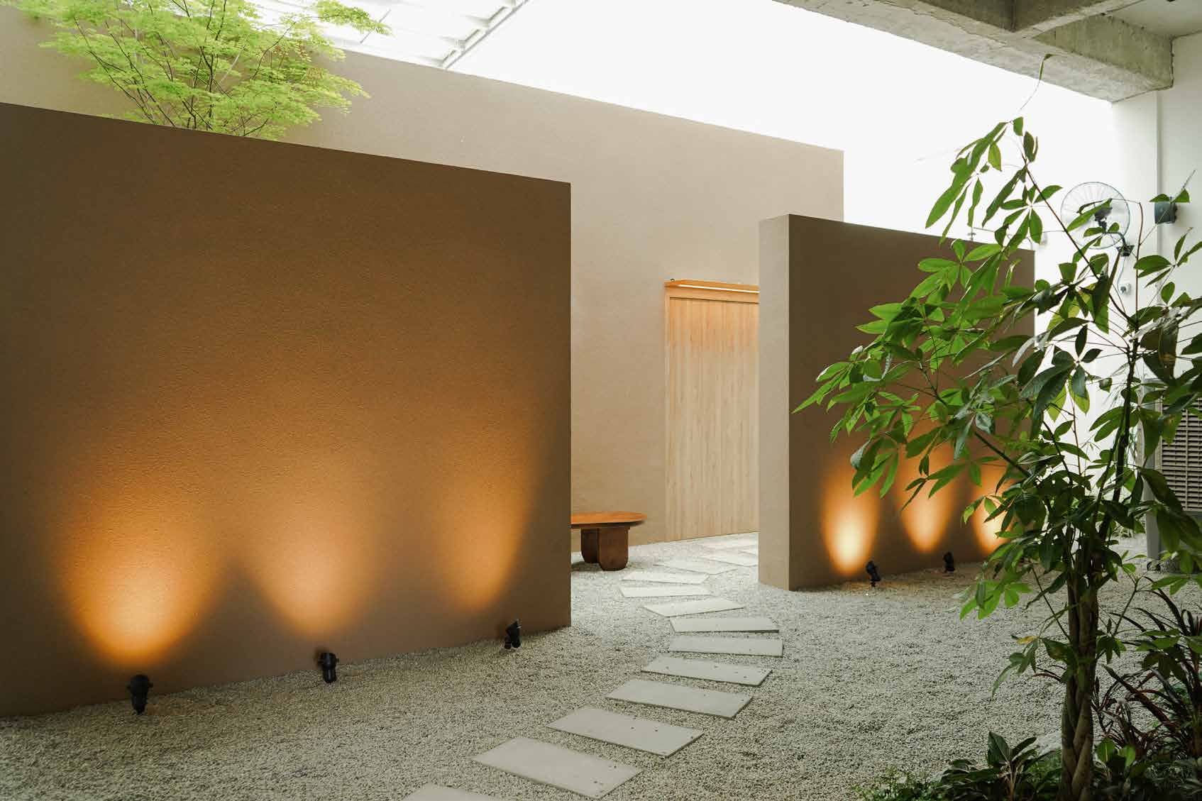 Up-lit clay walls and a stepping-stone path across white gravel in the entrance courtyard
