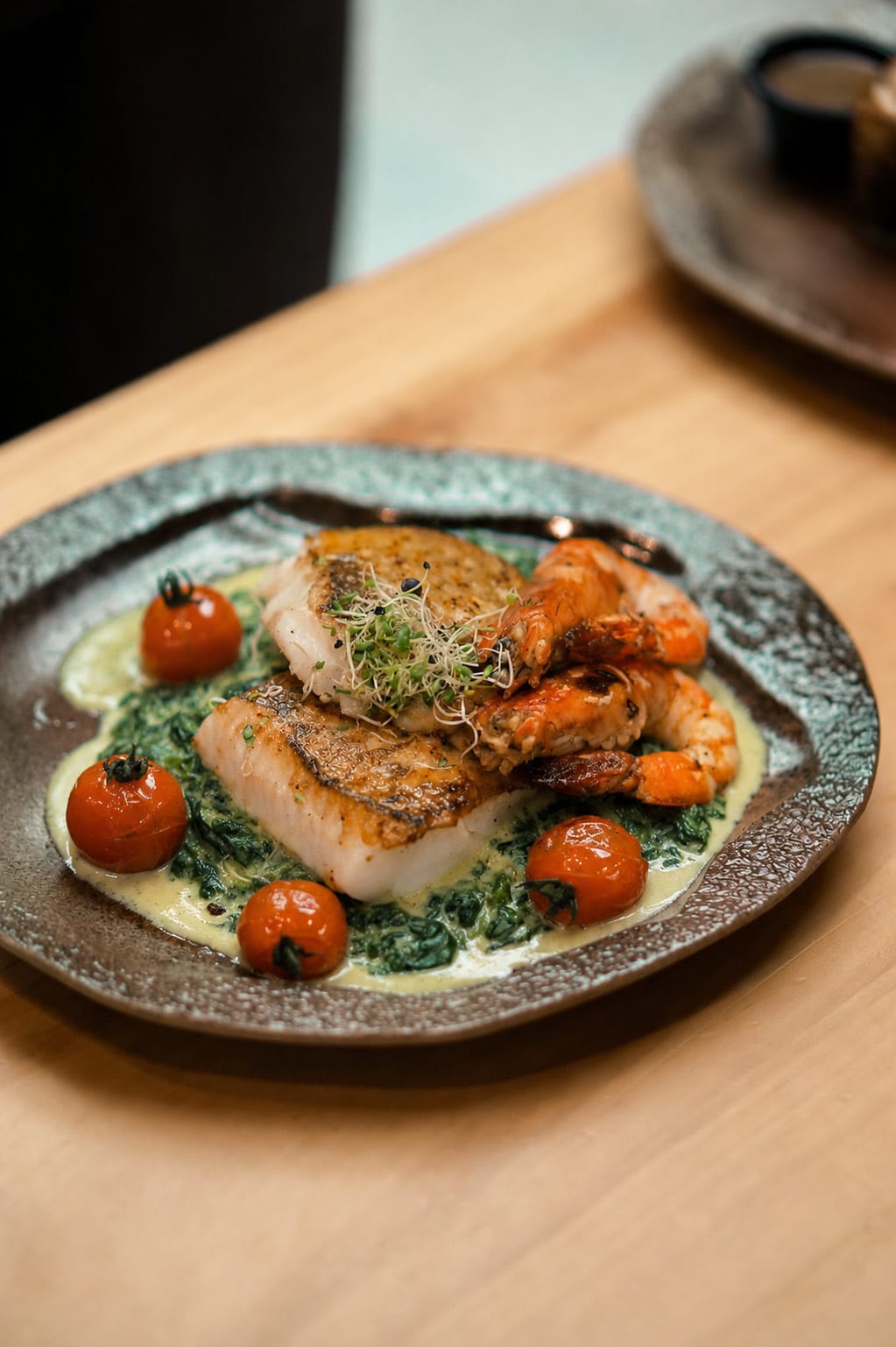 Garlic Miso Halibut with tiger prawns on creamy spinach, ringed by confit tomatoes