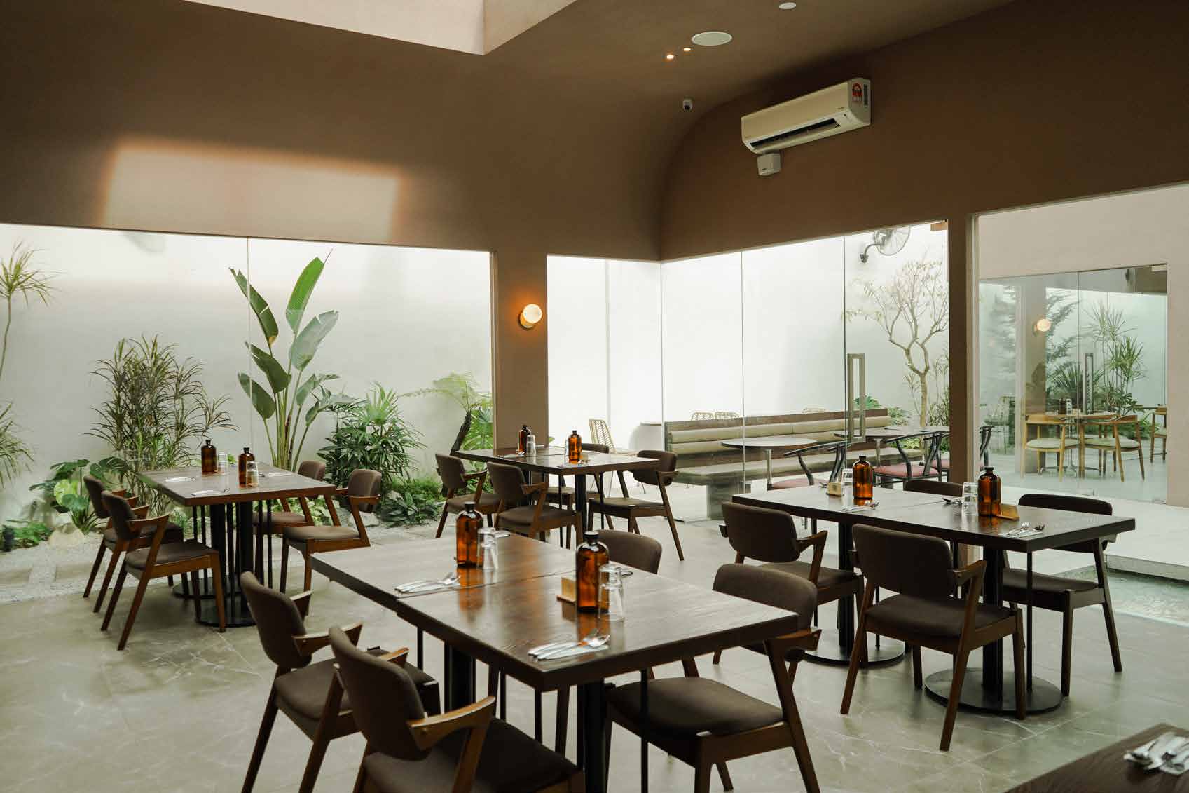 The Lounge Area: dark wood tables under a curved ceiling, with glass walls onto a planted light well