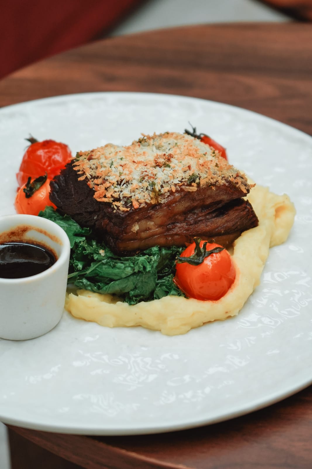 Herb-crusted braised Wagyu beef Karubi on mashed potatoes with roasted cherry tomatoes and a pot of jus